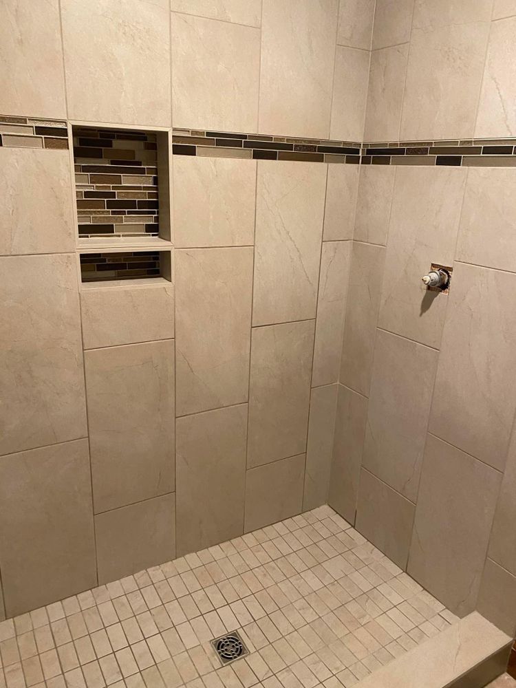 Empty tiled shower with a small wall shelf and floor drain