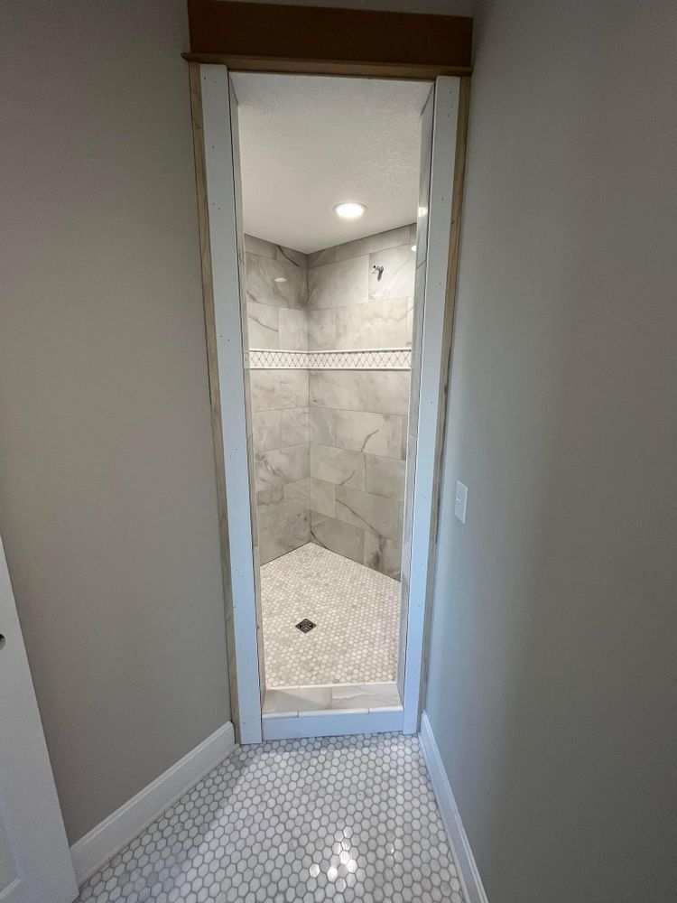 Narrow hallway entrance to a tiled shower room with white walls and recessed light