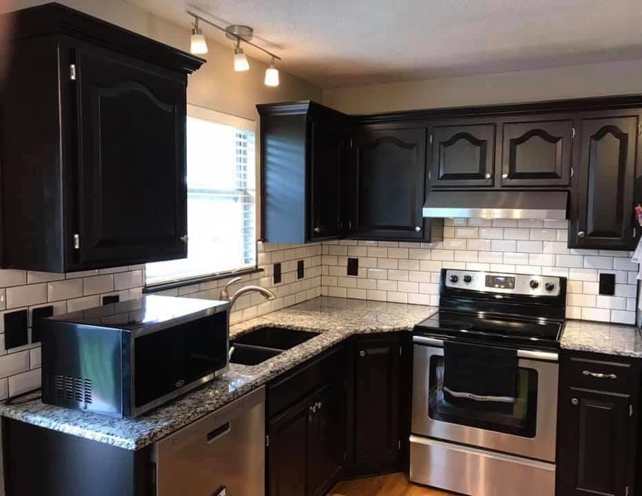 Black kitchen with stainless steel stove, dark cabinets, white tile backsplash, and granite counters.