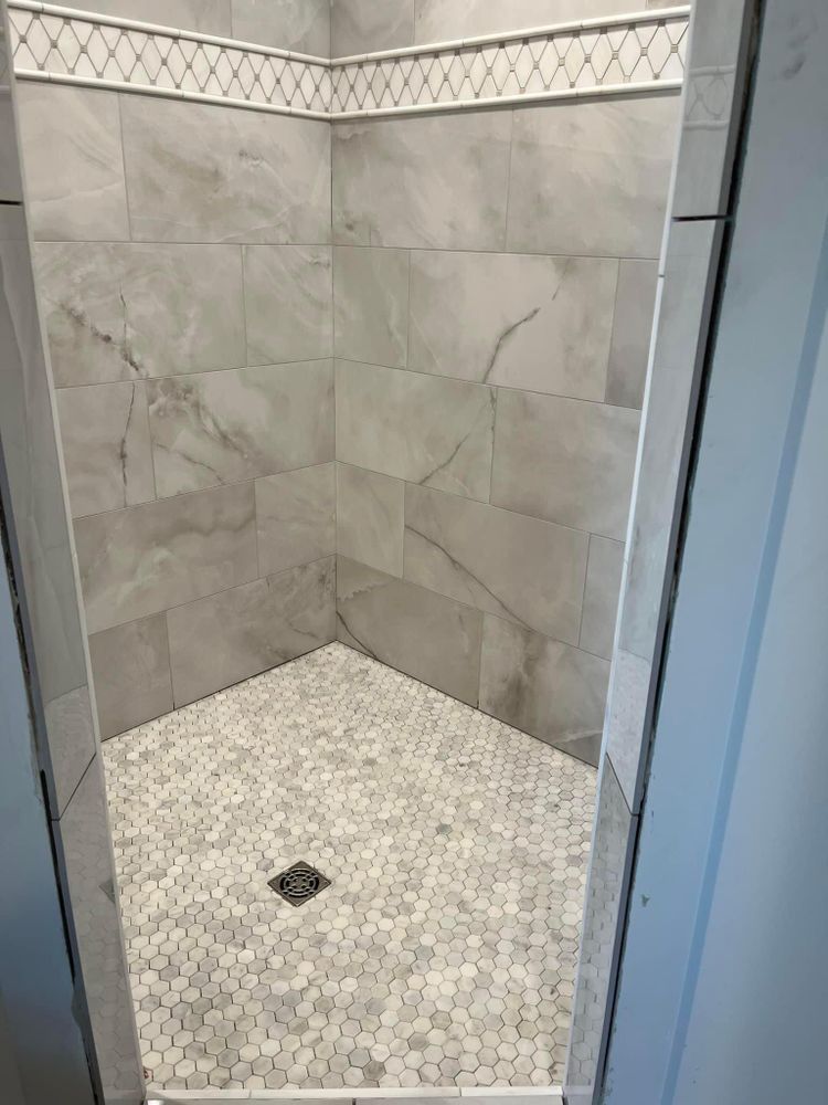 Tiled shower stall with gray wall tiles, mosaic floor, and decorative border trim