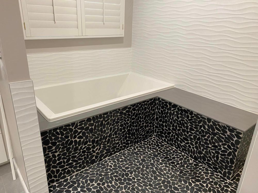 Black-and-white tiled bathtub alcove with white tub and textured white walls