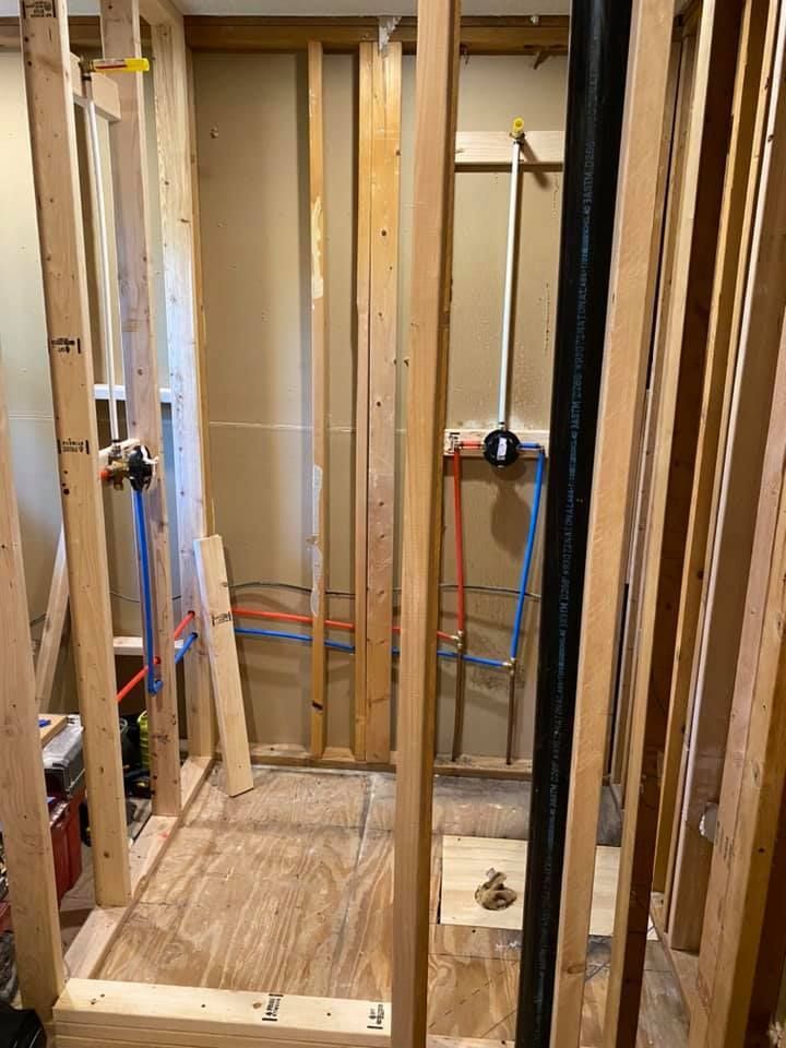 Unfinished bathroom framing with exposed studs, plumbing lines, and subfloor opening.
