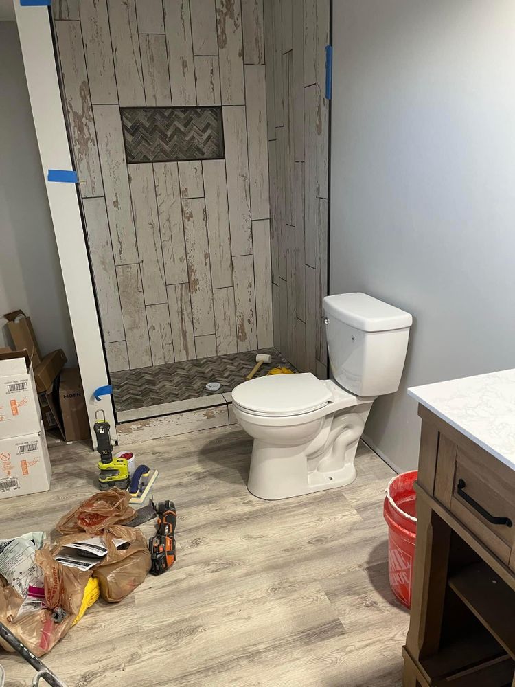 Small bathroom under renovation with a toilet, tiled shower wall, and supplies on the floor.