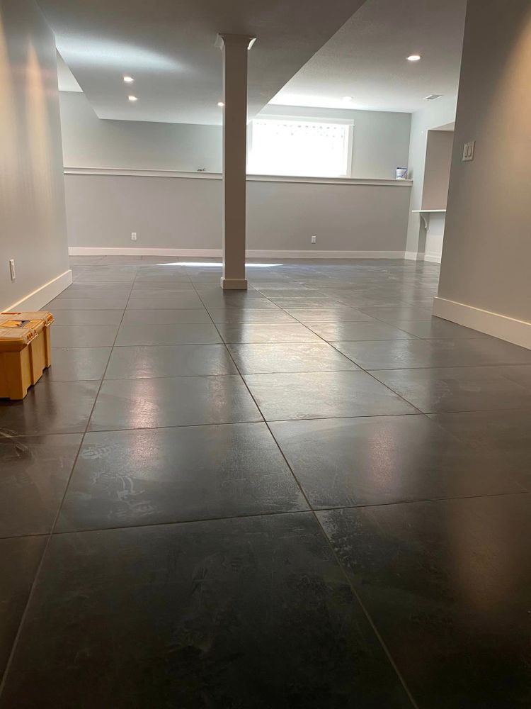 Empty tiled room with gray walls, a central support column, and a bright windowed opening at the back.
