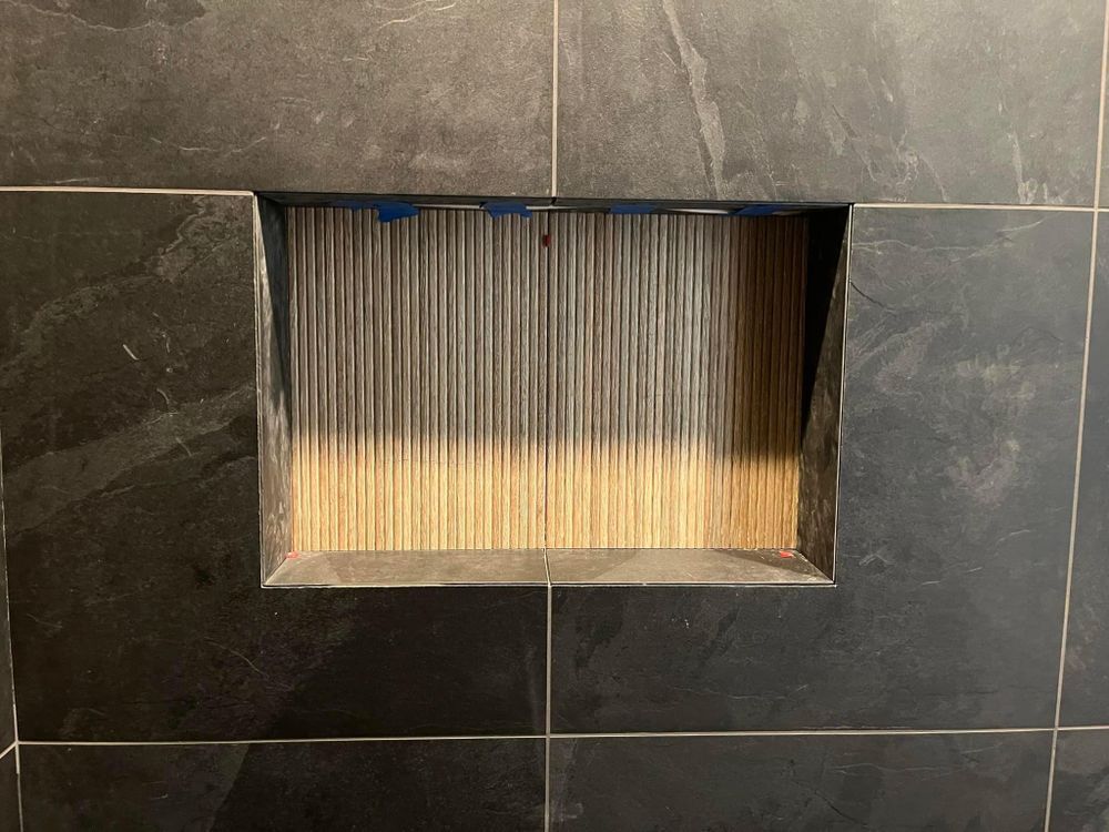 Recessed wall niche with ribbed glass panel set in dark gray tile.