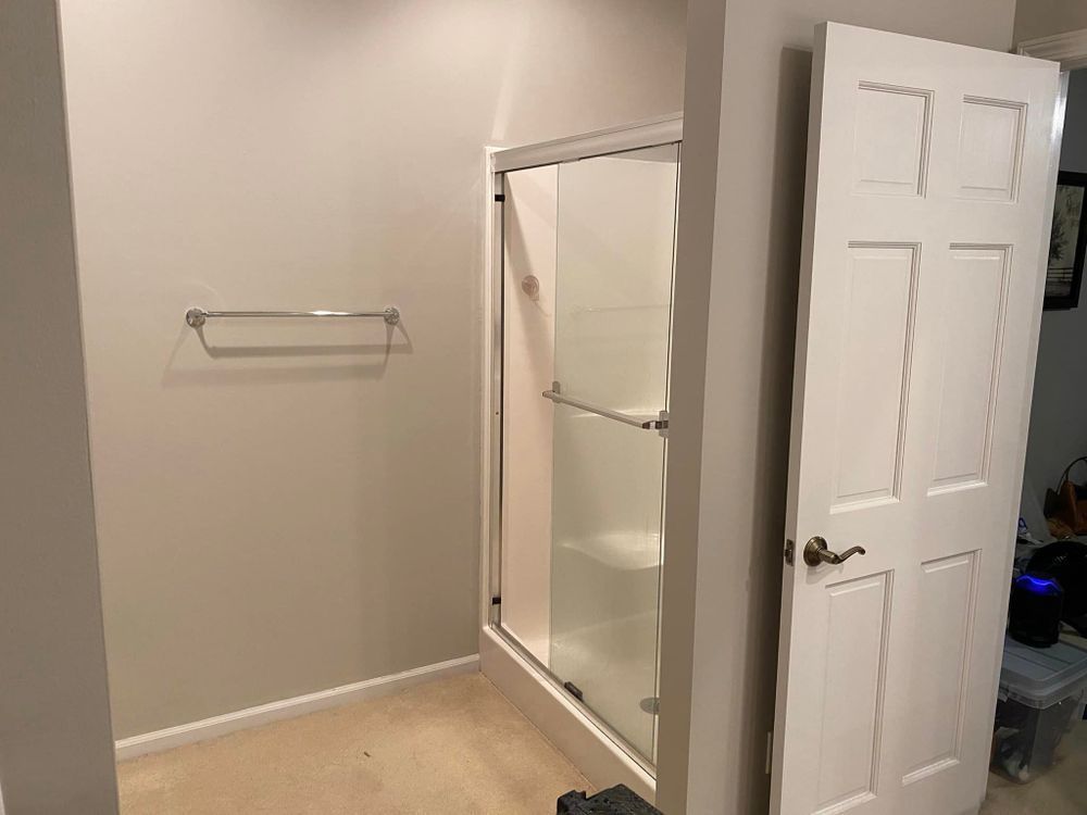 Empty bathroom with open white door, shower stall, and towel bar on beige walls.