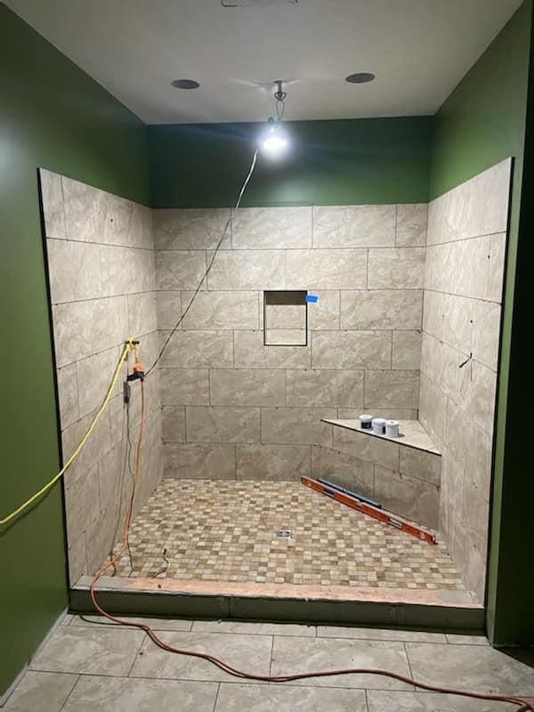 Partially tiled shower under construction with green walls, exposed wiring, and a bright ceiling light