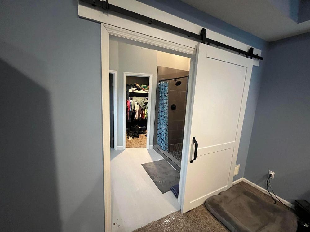 Sliding barn door opening to a walk-in closet with hanging clothes and a tiled bathroom beyond.