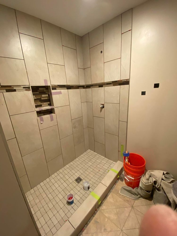 Partially tiled bathroom under renovation, with open wall cutouts, a shower floor, and a red bucket on the floor