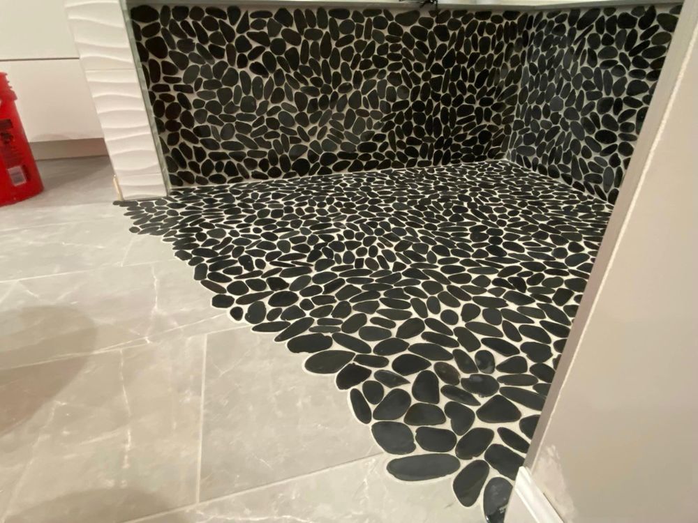 Black pebble-tile shower floor and back wall in a bathroom with white walls and a gray tile floor
