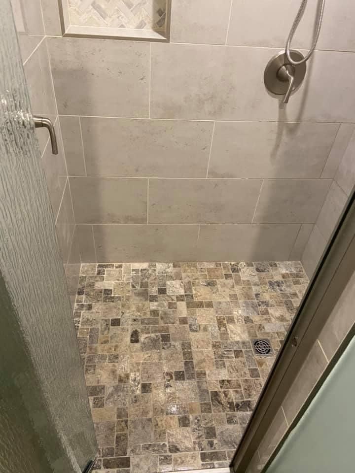 Small tiled shower with gray walls, mosaic floor, glass door, and chrome shower controls.