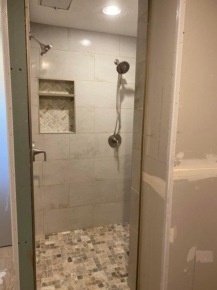 Small tiled shower stall with built-in shelf, dual showerheads, and mosaic floor.