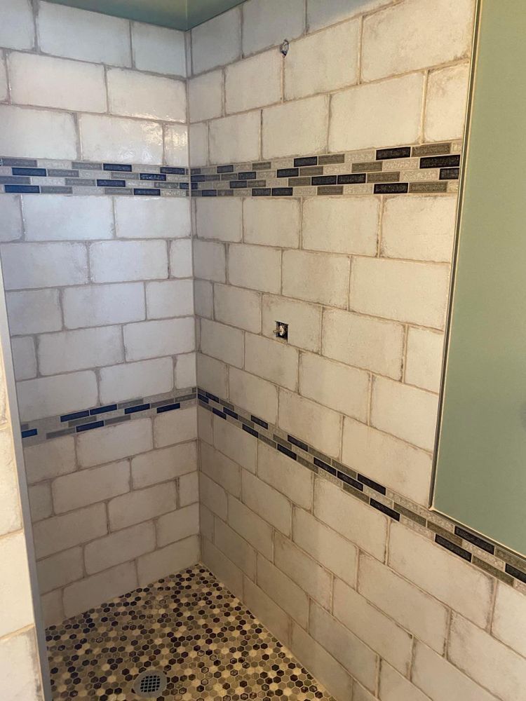 Tiled shower stall with white walls, dark mosaic border, and patterned floor tiles
