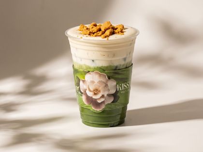 Green layered dessert drink with whipped cream and crumb topping in a clear cup, decorated with a flower