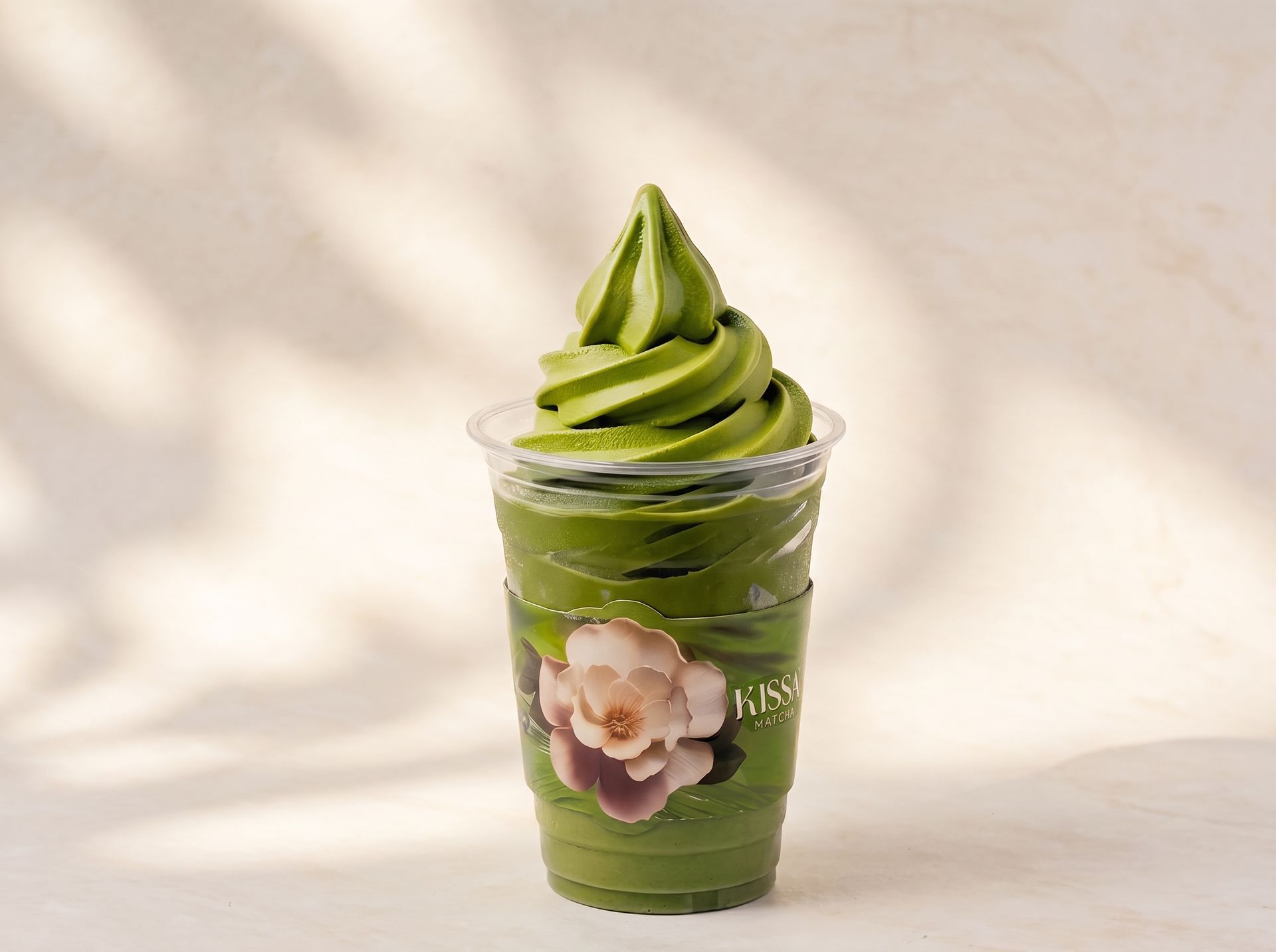 Clear cup of green soft-serve topped with swirls, decorated with a flower sticker, on a light background