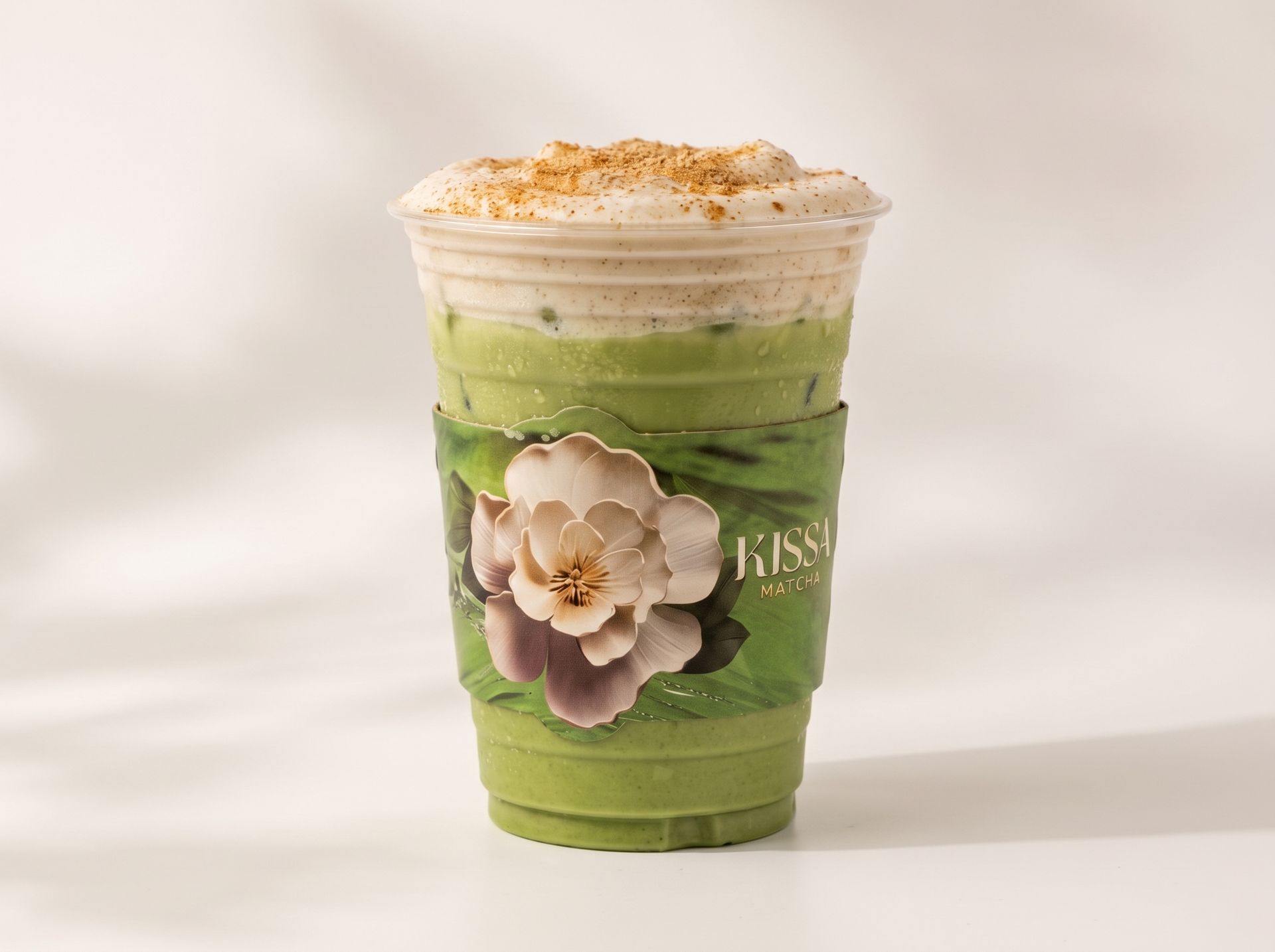 Green iced drink in a clear cup with whipped topping, cinnamon dusting, and a flower decoration