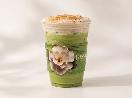 Green iced drink in a clear cup with whipped topping, cinnamon dusting, and a flower decoration