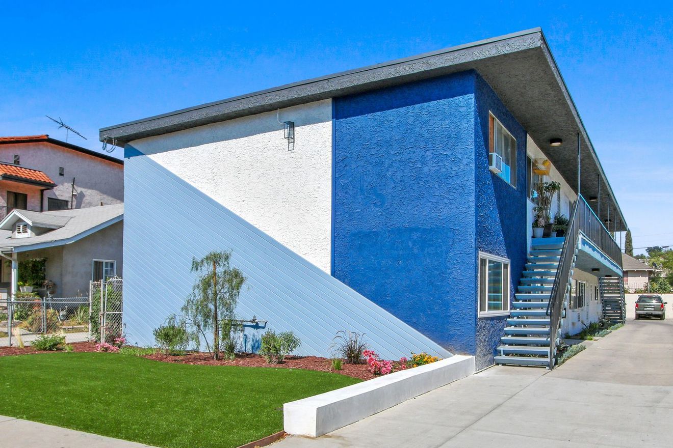 Blue and white apartment building with stairs, walkway, and landscaped lawn on a sunny day
