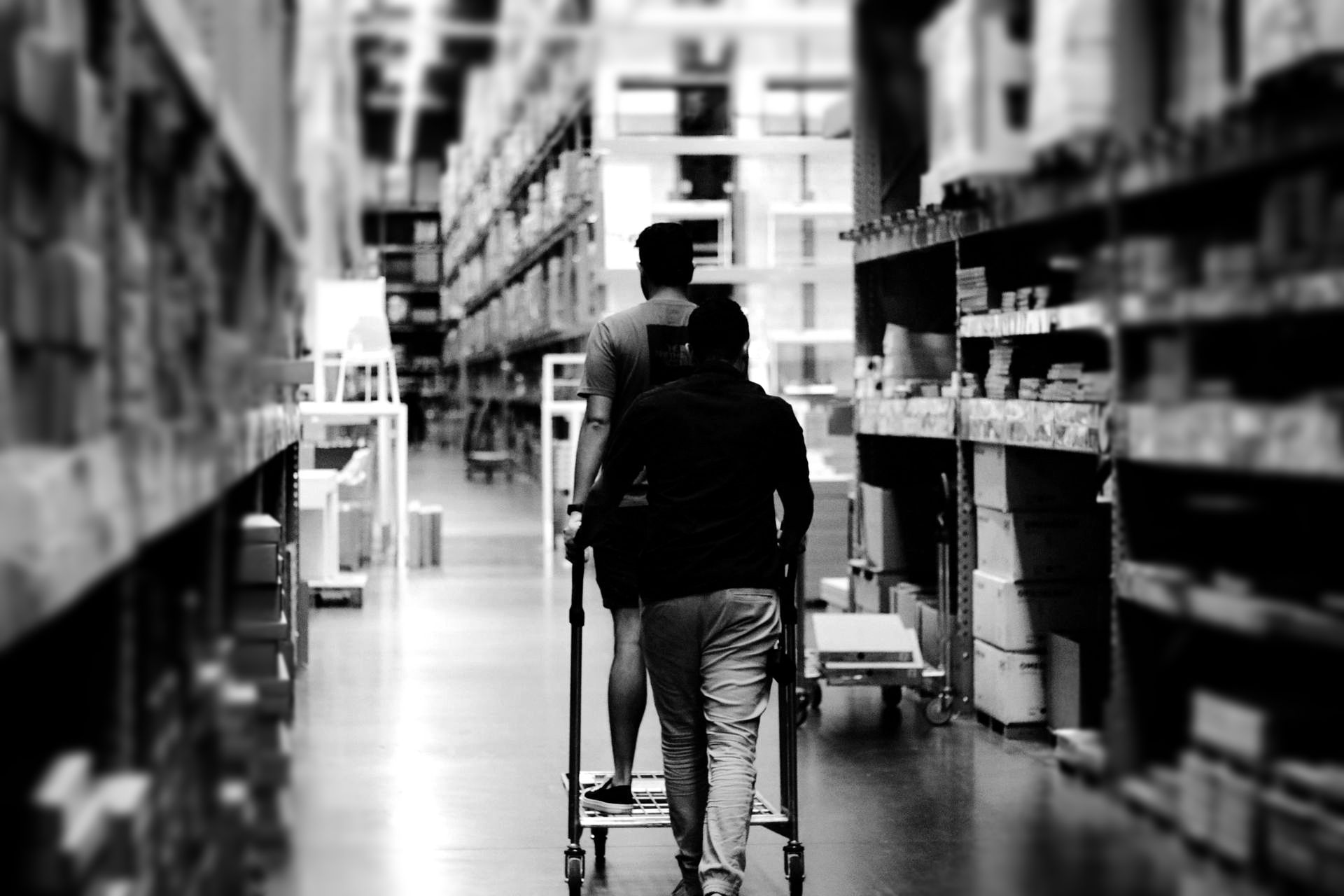 Person pushing a shopping cart down a store aisle in black and white.