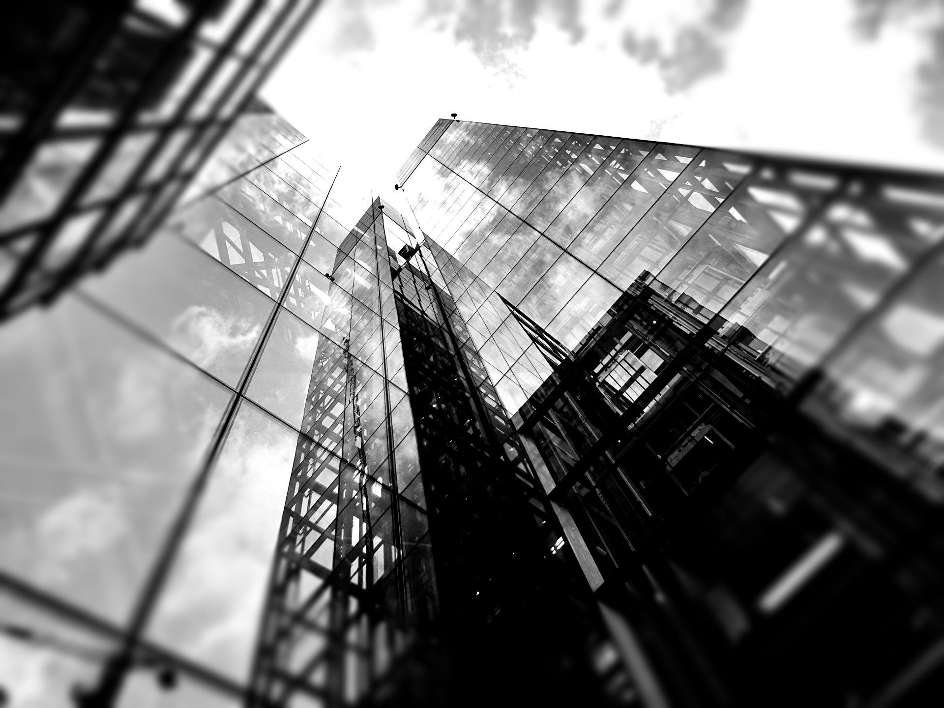 Black-and-white upward view of modern glass skyscrapers against a cloudy sky