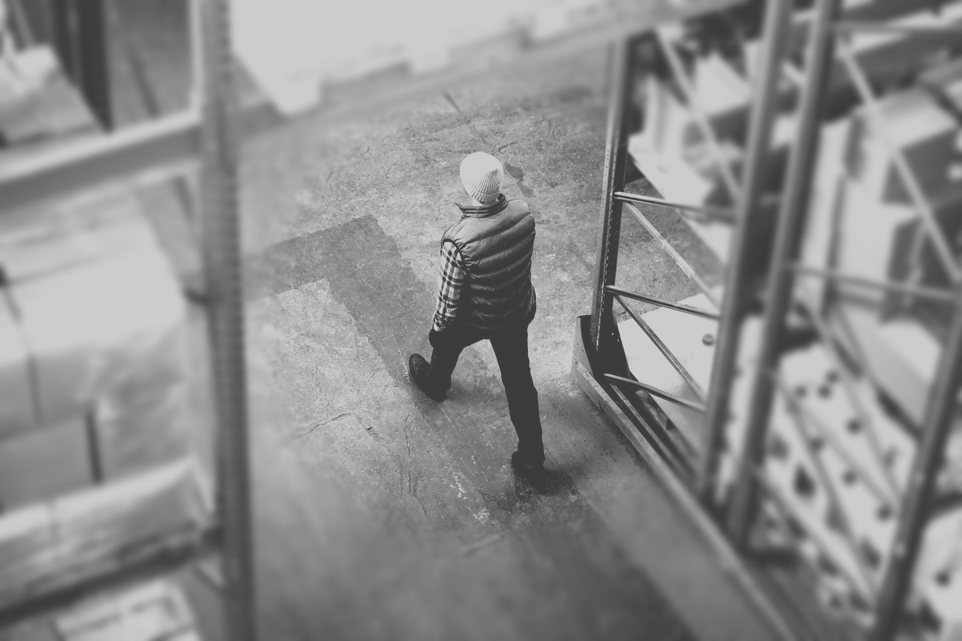 Person walking through a warehouse aisle carrying a bag or box, viewed from above.