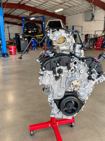 Car engine on a red stand in an auto repair shop, with lifts and another vehicle in the background
