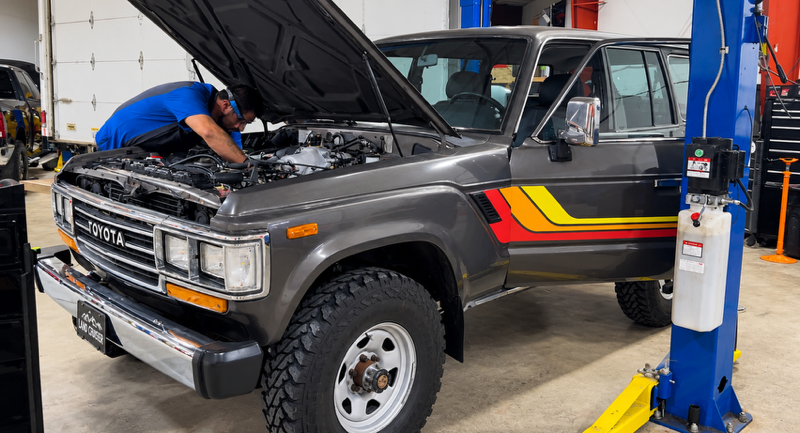 Mechanic working under the hood of a gray SUV in a repair shop