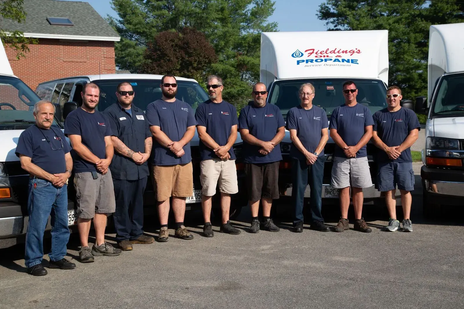 Eight people in navy shirts stand beside a truck and trailer with a company logo outdoors.