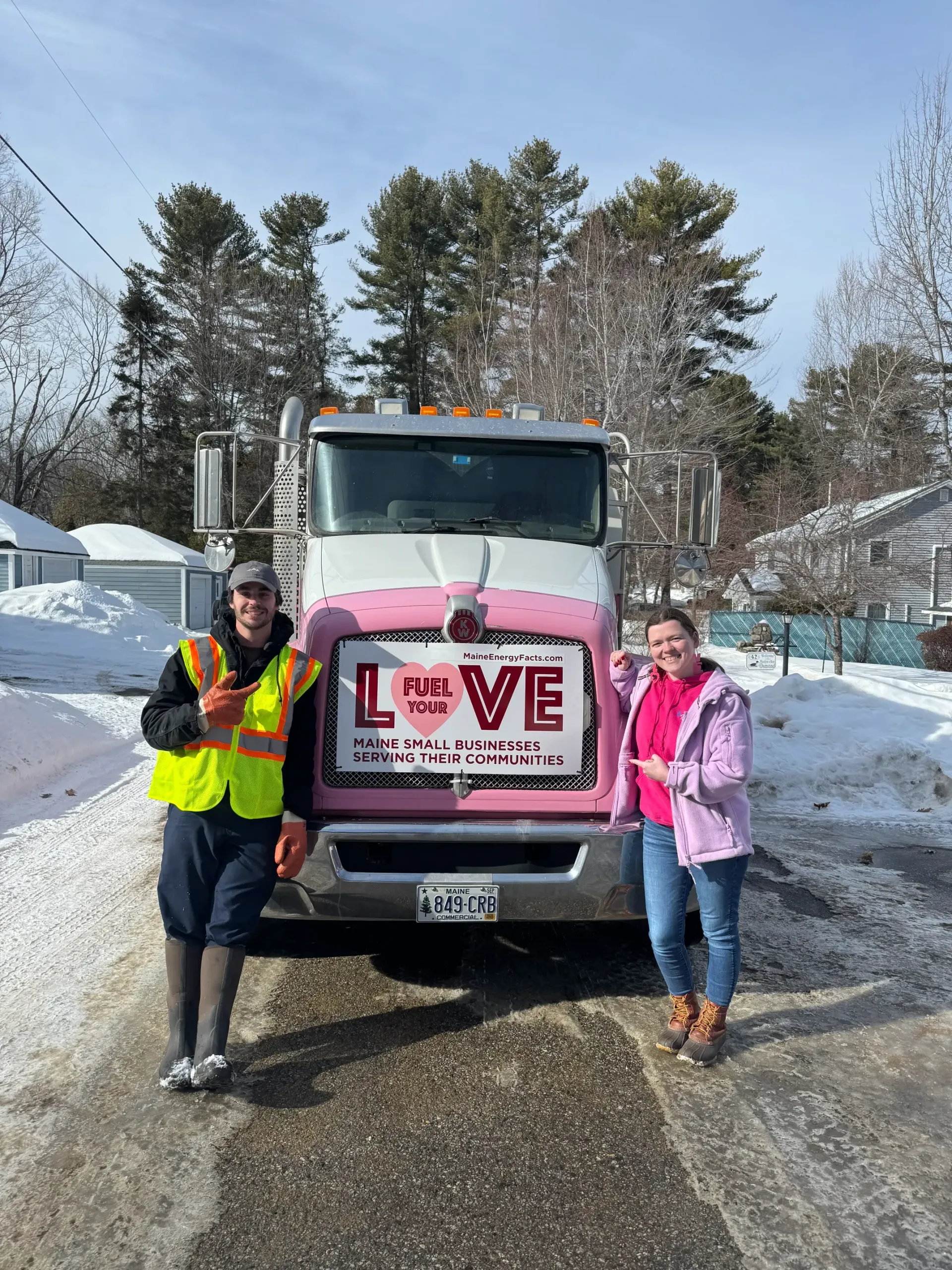 Two people standing beside a pink truck with a “LOVE” sign on a snowy road.