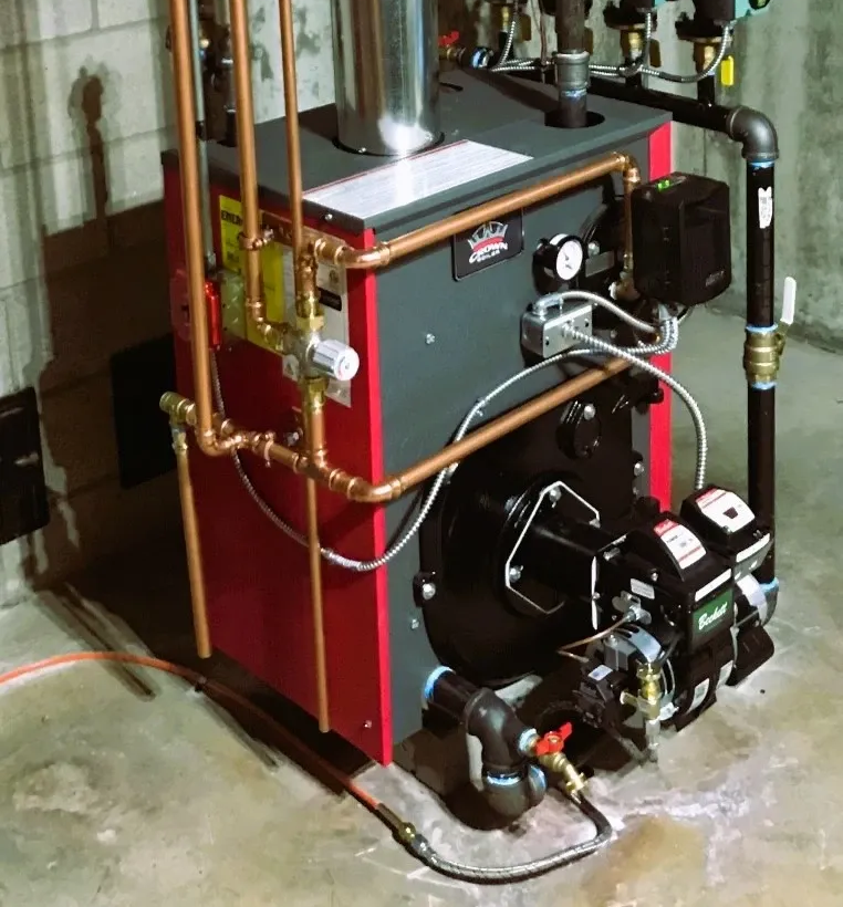 Basement utility room with a red boiler, exposed pipes, and heating equipment on the floor.