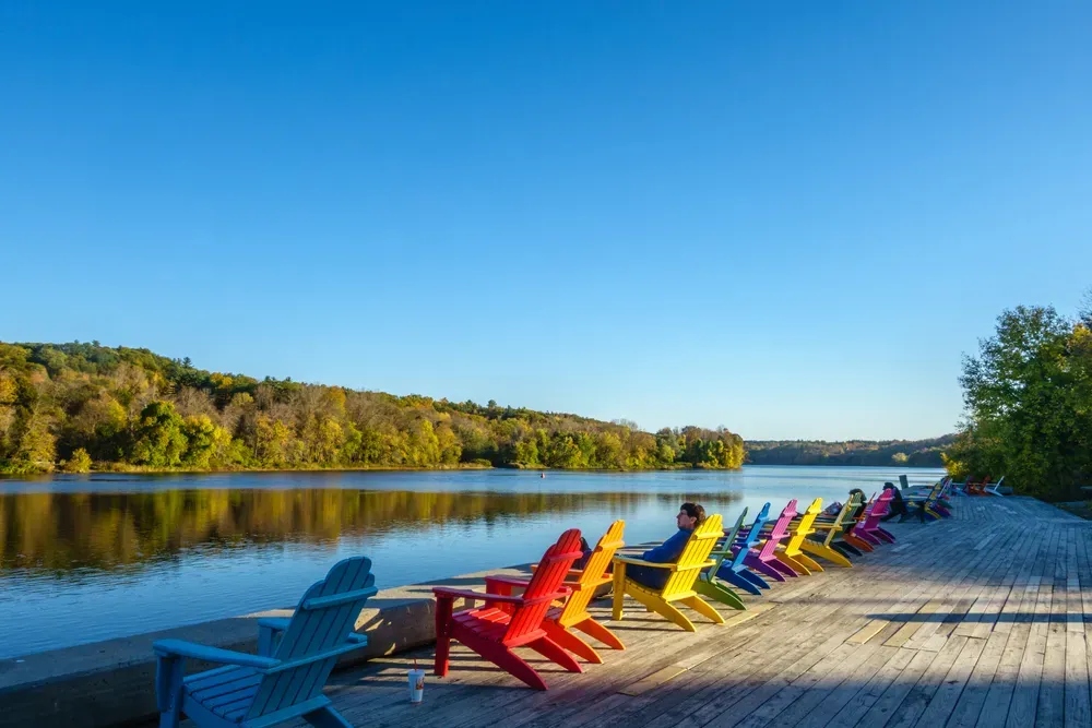 Colorful Adirondack chairs on a wooden dock beside a calm lake under a clear blue sky