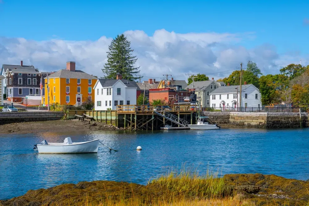 Colorful waterfront houses and boats along a calm harbor under a bright sky