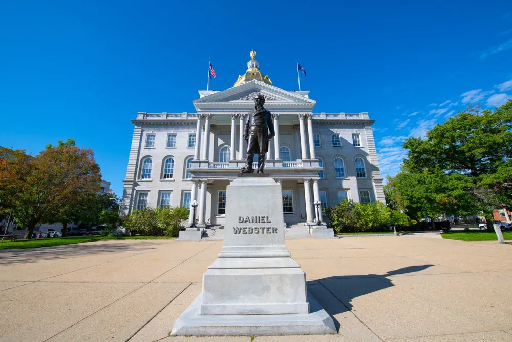 Statue of Daniel Webster before a white neoclassical building under a bright blue sky