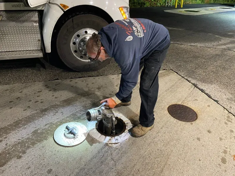 Worker inspecting an open manhole beside a truck on a city street