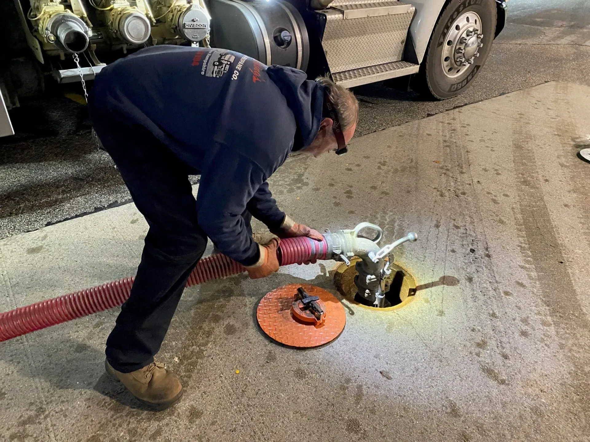 Worker using a power tool to open a manhole on a road beside a truck