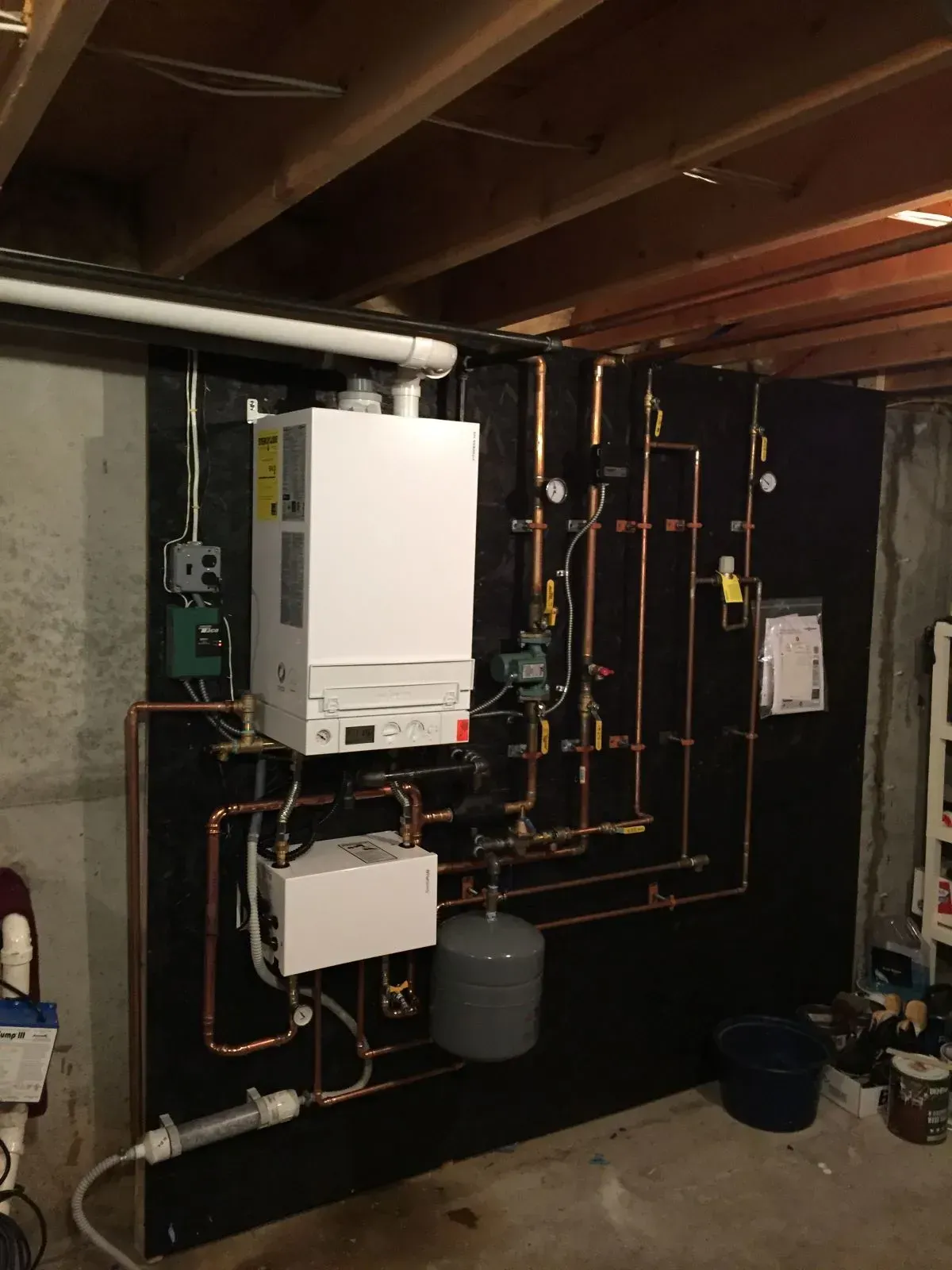 Basement utility room with a wall-mounted boiler, copper pipes, and plumbing equipment above a concrete floor