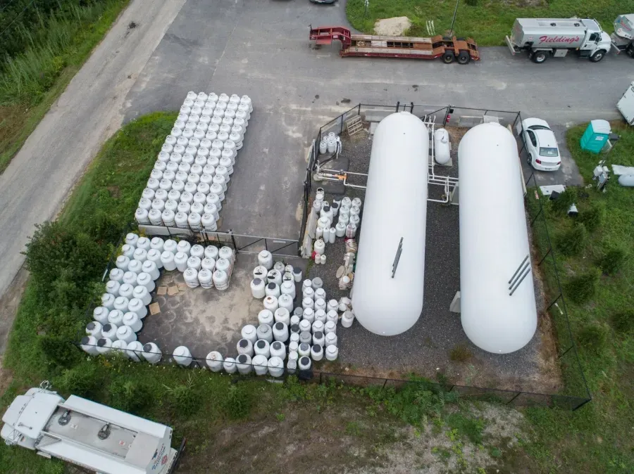 Aerial view of an industrial yard with large white tanks, stacked white cylinders, and parked trucks.