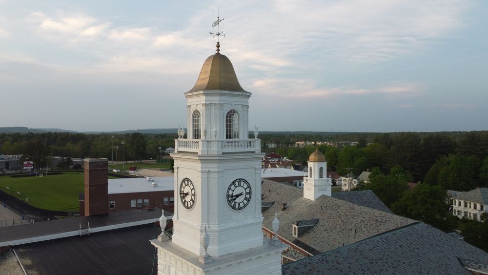 White clock tower with gold dome above a small-town skyline at sunset
