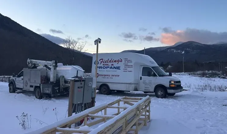 Snowy roadside with a white utility van, truck equipment, and mountains at dusk