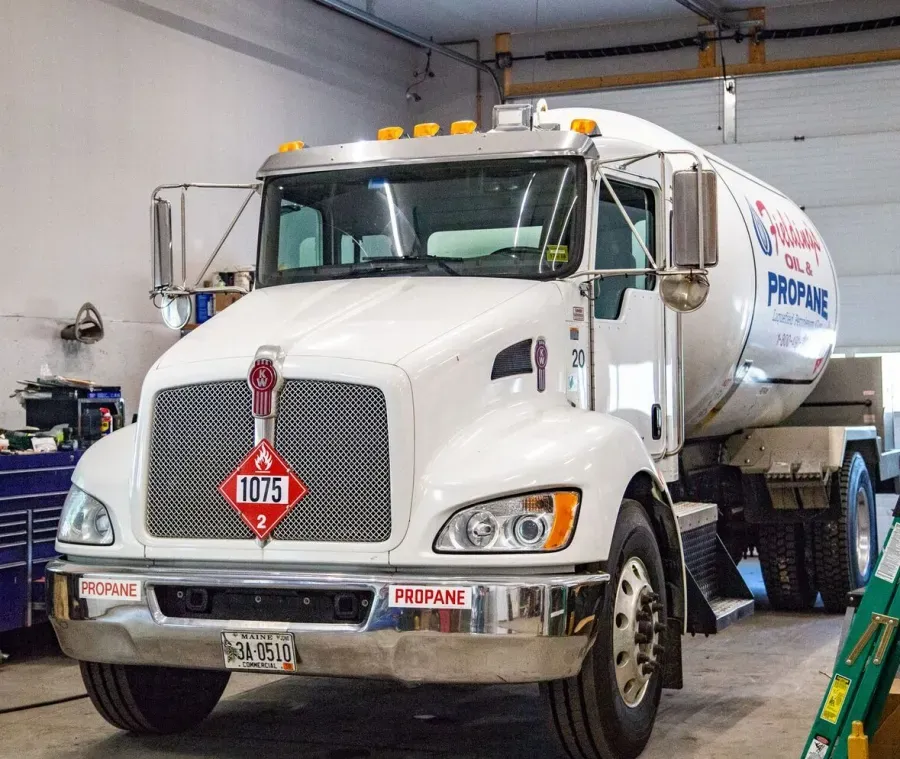White propane delivery truck parked inside a garage, front view with red hazmat placard.