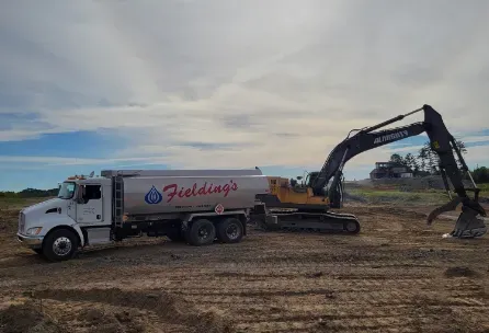 White dump truck and excavator at a dirt worksite under a cloudy sky