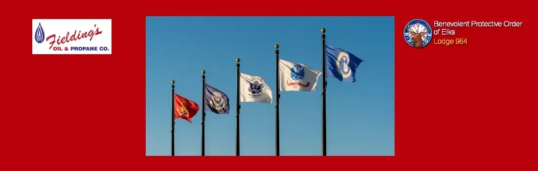 Four flags on poles against a blue sky, with logos in the top corners on a red banner background