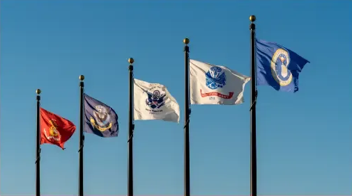 Five flags on tall poles waving against a clear blue sky.