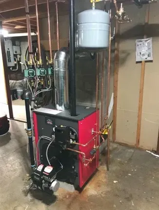 Red boiler/furnace in a basement utility room with silver ductwork and a blue water tank above.