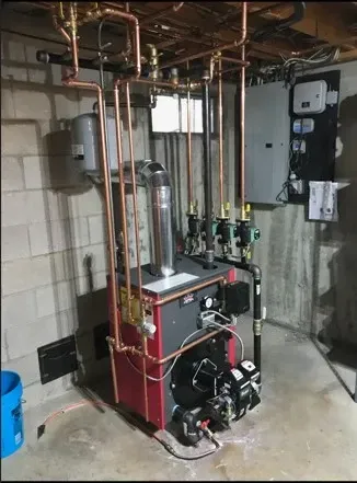 Basement utility room with red boiler, copper pipes, and water heater equipment.