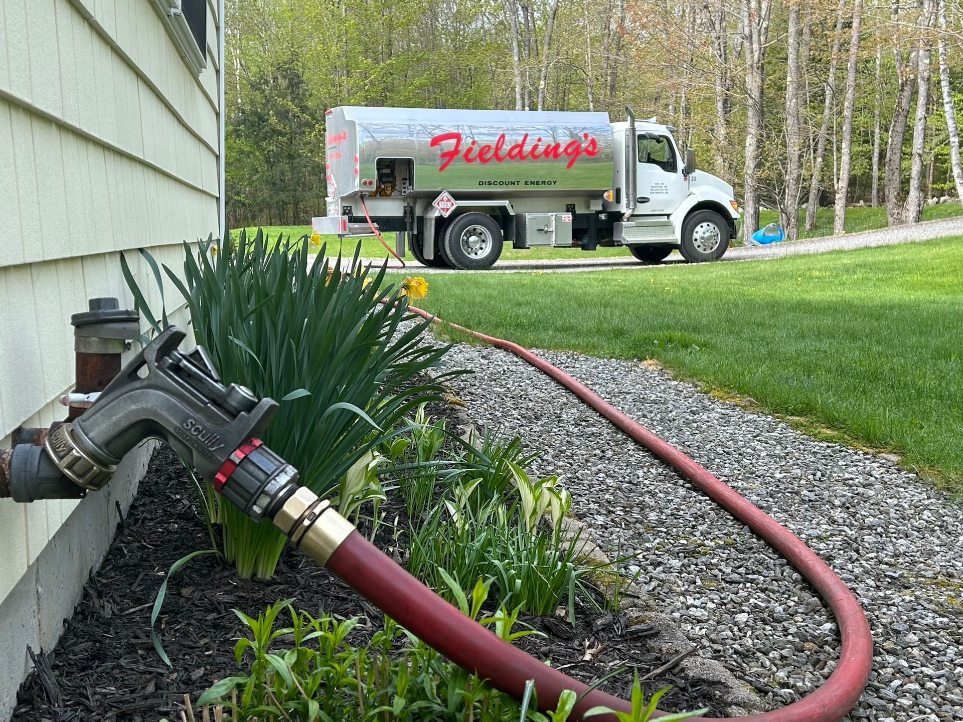 Fire truck connected to a house hose, water flowing through a red hose in a yard