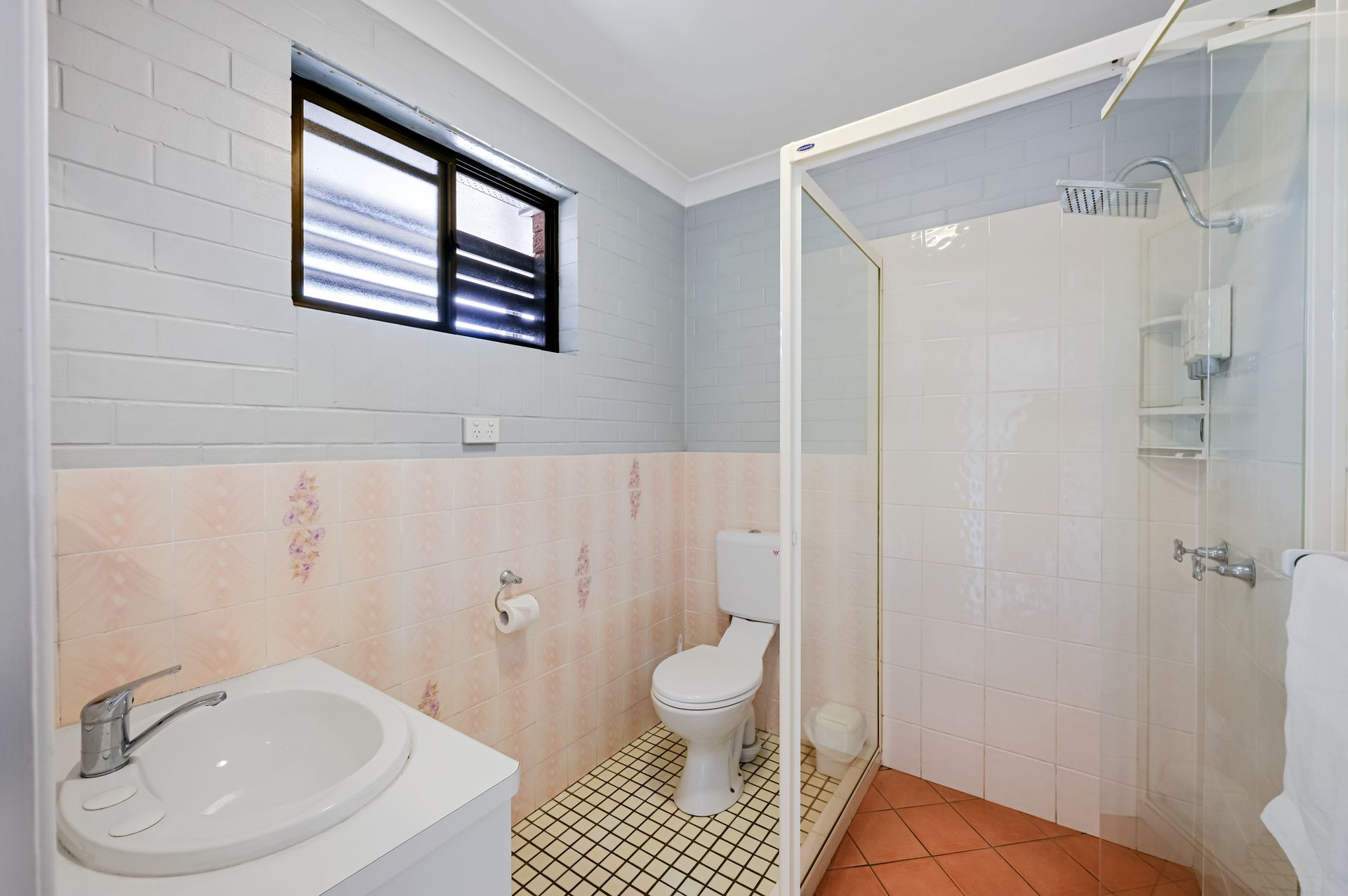 Bright bathroom with sink, toilet, and glass shower, tiled walls, and a small window.