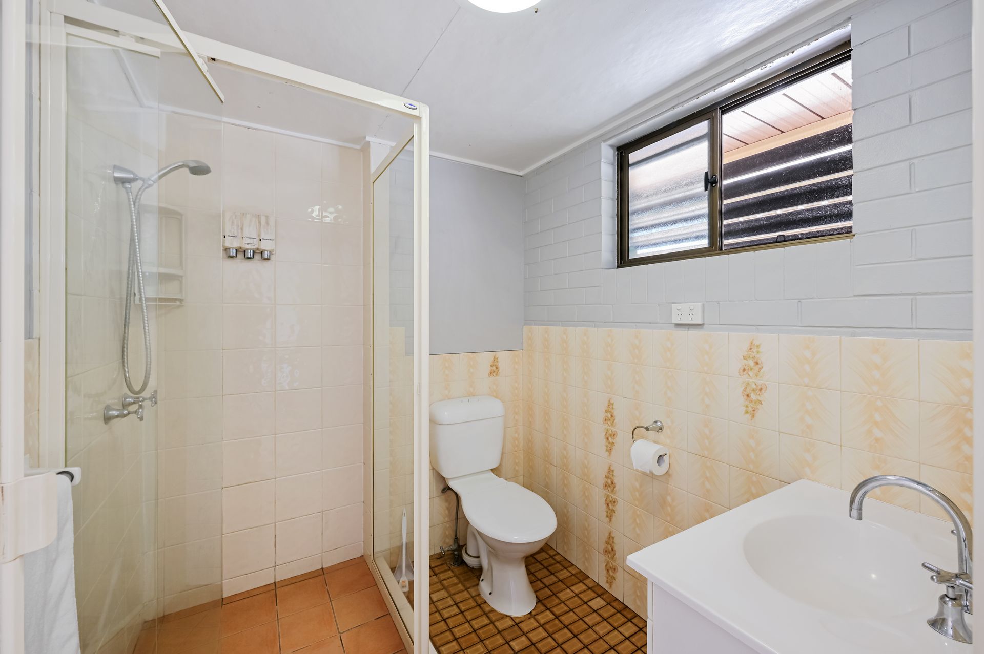 Small bathroom with shower, toilet, and sink, featuring white tile and light gray walls.