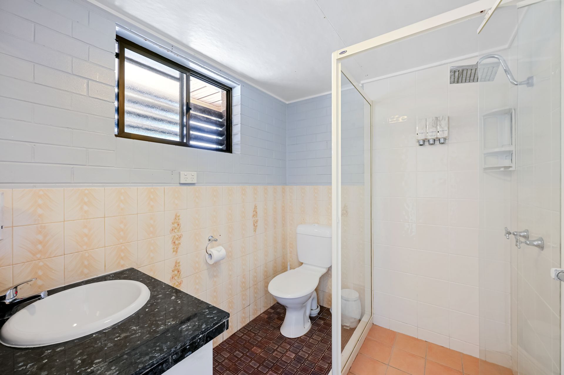 Small bathroom with sink, toilet, shower, blue tile walls, and a black window blind.