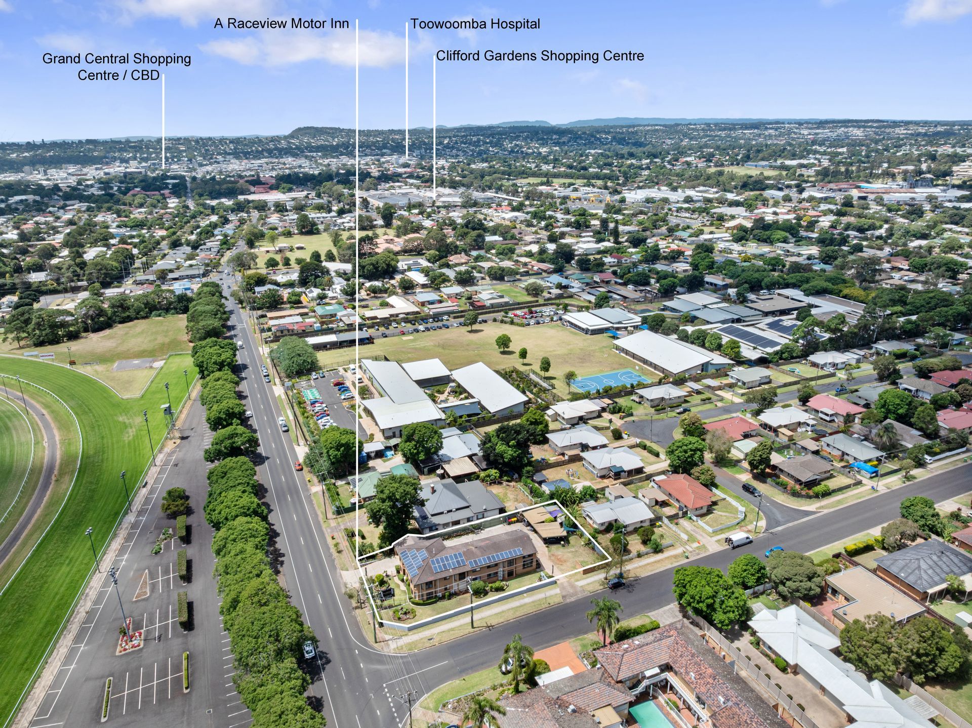 Aerial view of a suburban neighborhood with roads, houses, and green hills under a clear sky